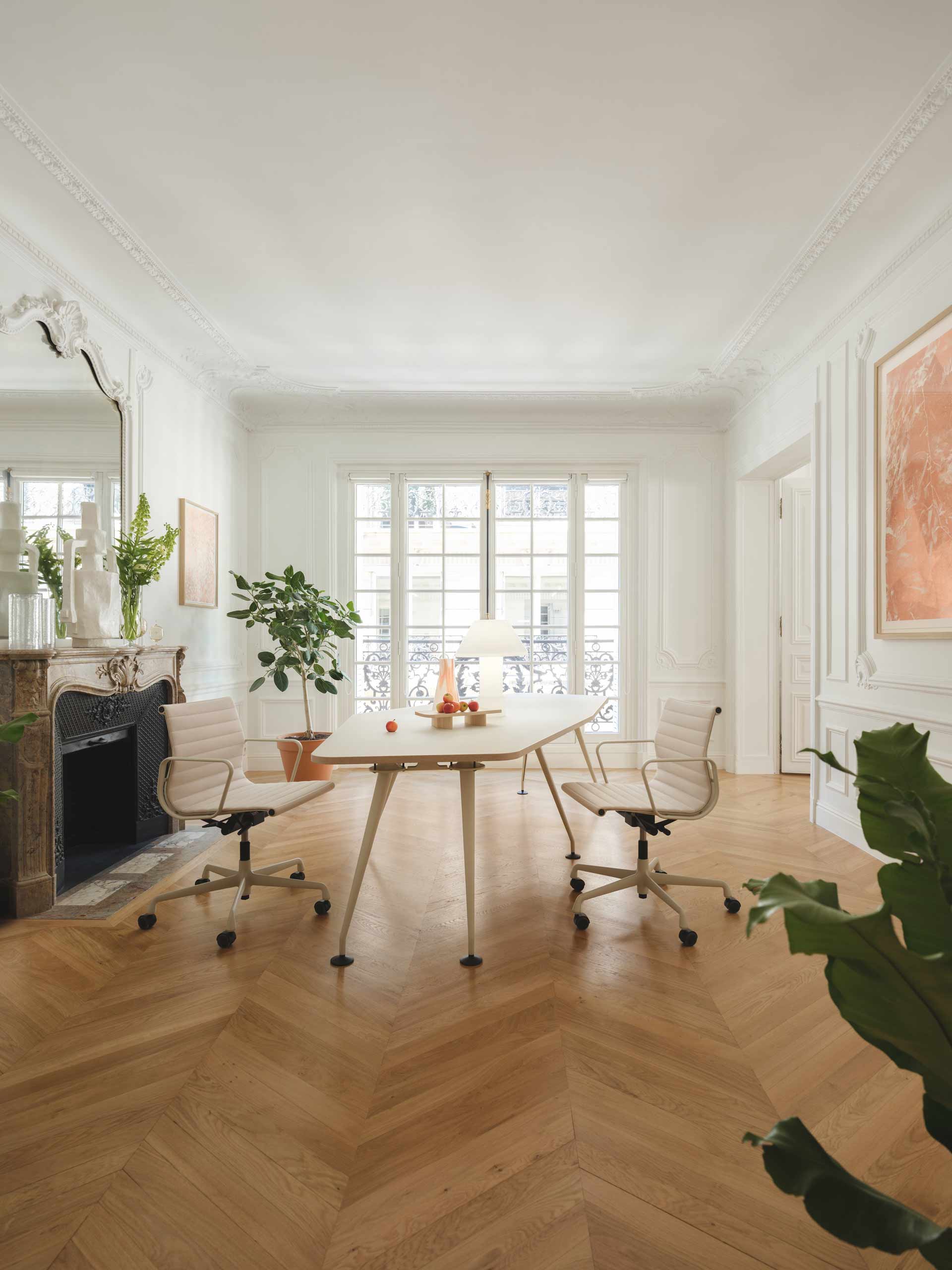 Une salle de réunion prestigieuse met en scène une table effilée et des fauteuils de bureau blancs face à une cheminée ancienne et une grande fenêtre parisienne.