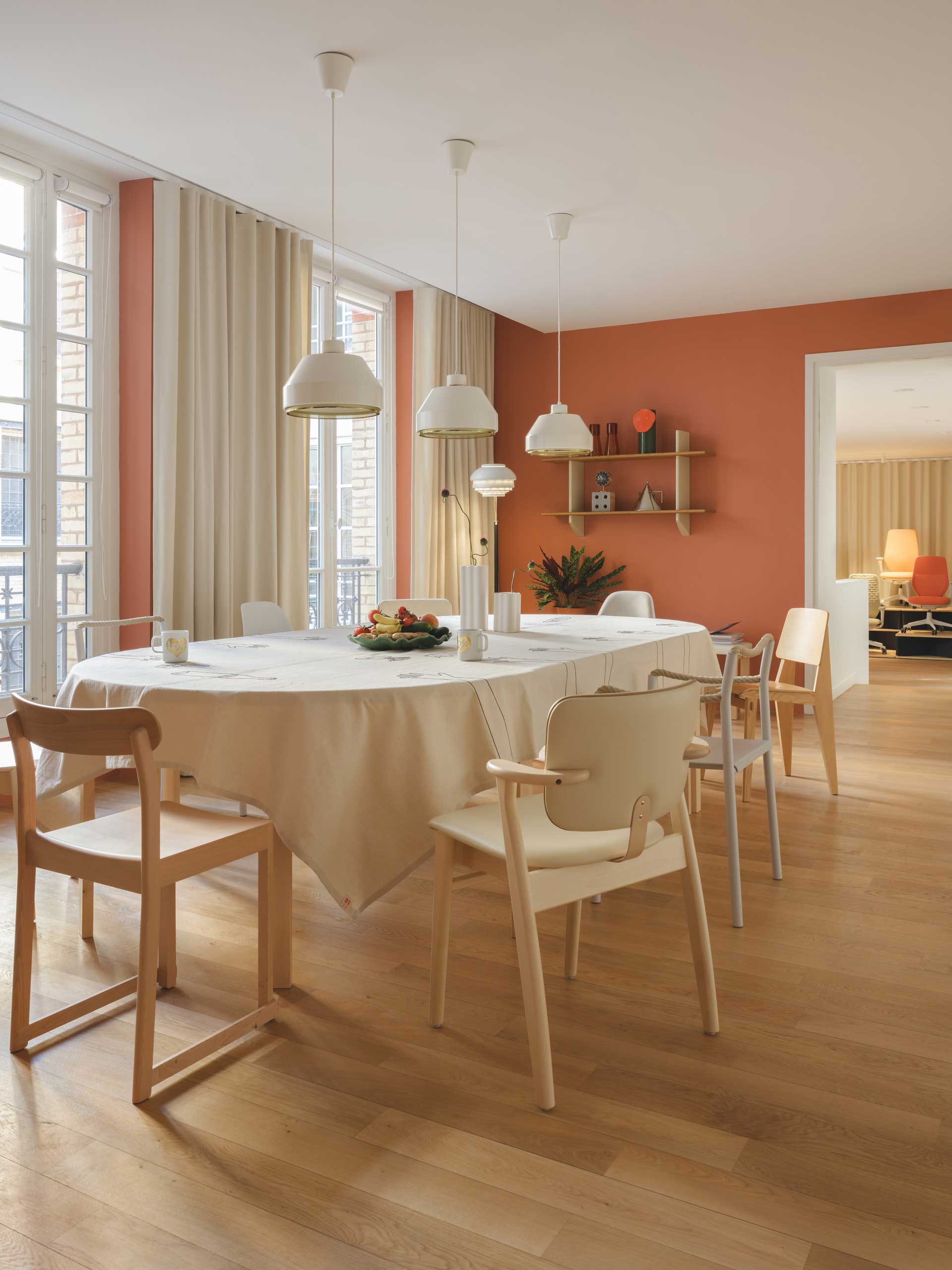 Une table de réunion conviviale recouverte d'une nappe blanche est entourée de chaises en bois clair dans une pièce aux murs terracotta et blanc.