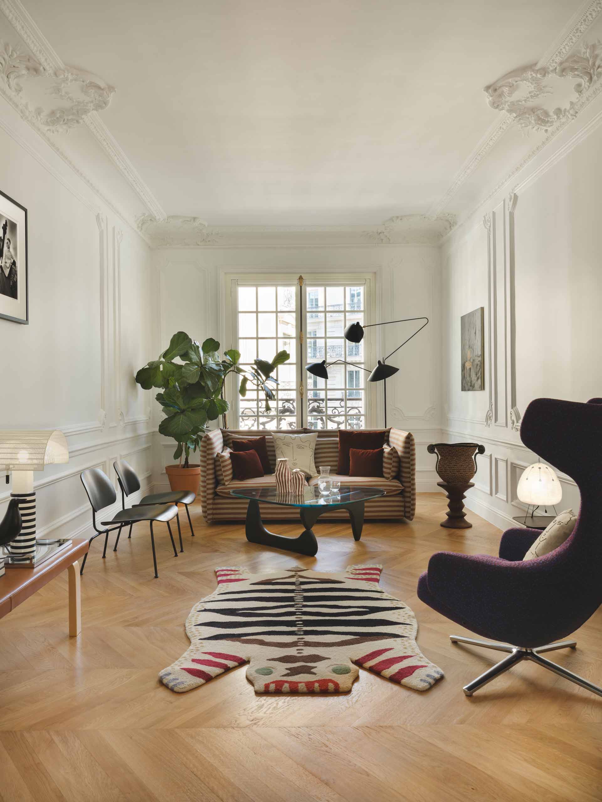 Ce salon au style haussmannien mélange mobilier iconique et touches ludiques, avec un tapis en forme de tigre et une table basse Noguchi au centre.