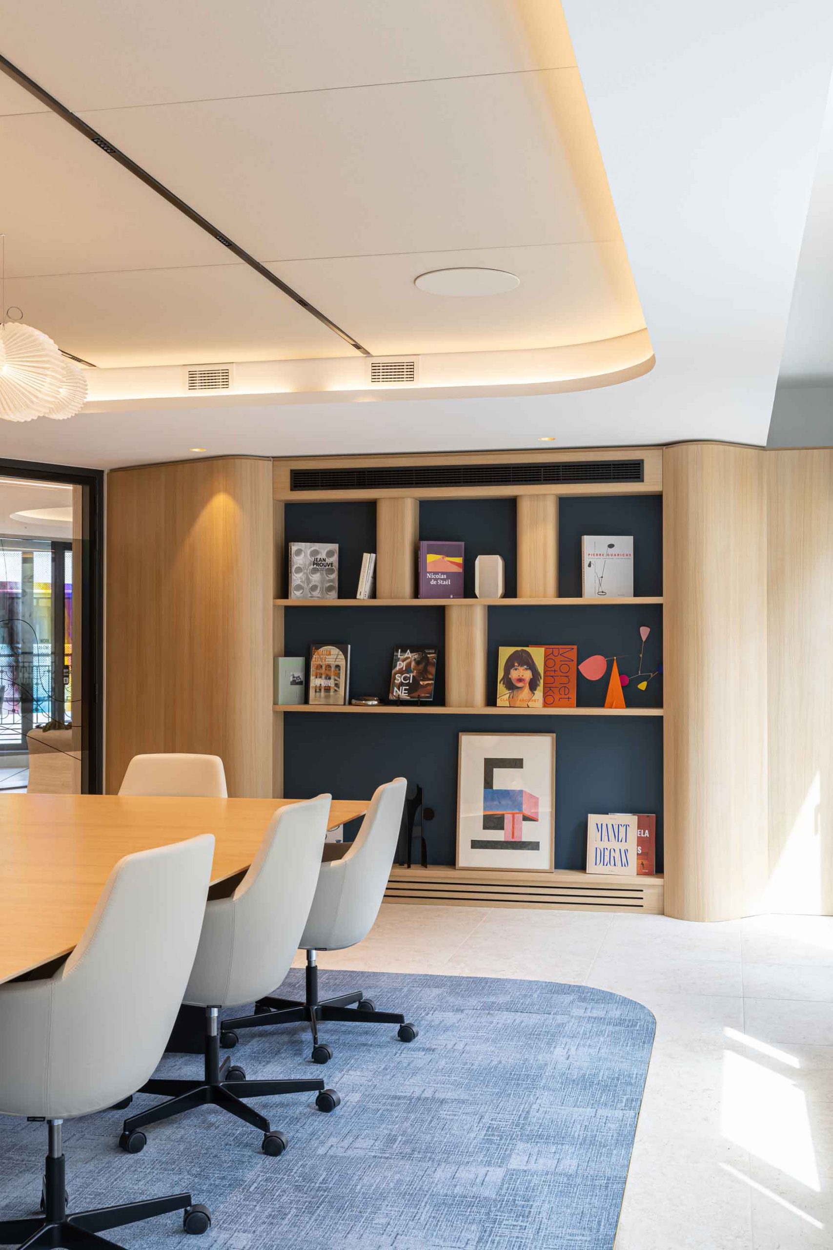 Détail d'une bibliothèque encastrée dans un mur bleu foncé, présentant des livres d'art (Rothko, Monet, Degas) et des objets décoratifs.