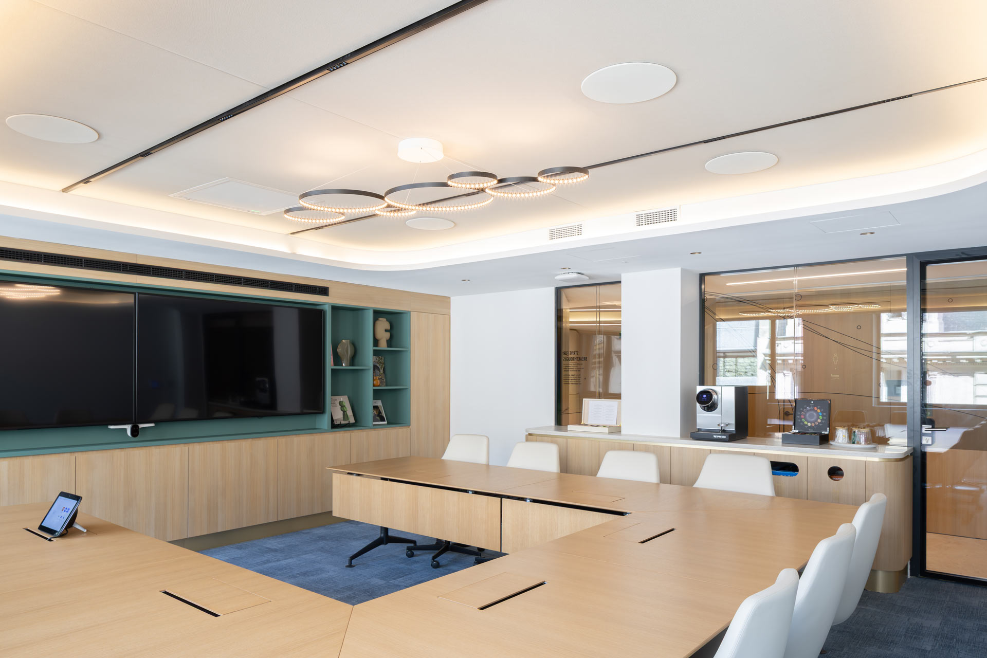 Une autre salle de réunion équipée de deux grands écrans muraux, d'une table modulaire en bois et d'un luminaire circulaire moderne au plafond.